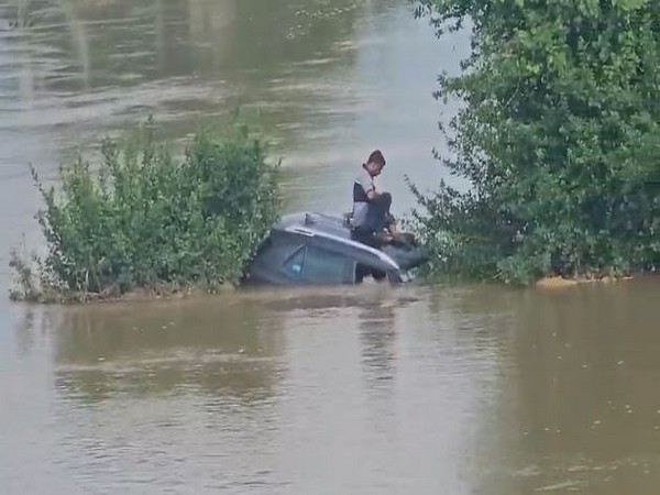 Men shelter over car roof after it stuck on inundated road (Photo/ANI)