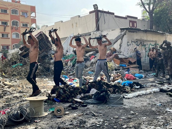 Men holding raised weapons are led out by Israeli soldiers in the northern Gaza Strip (Photo Credit: Reuters)