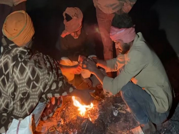 People huddled around a bonfire to ward off the cold. (Photo/ANI)