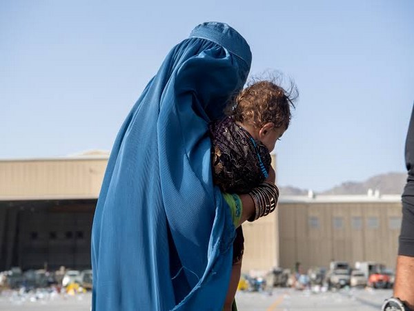 A woman carries a child at Hamid Karzai International Airport in Kabul, Afghanistan (Photo Credits: Reuters) 
