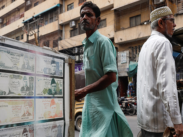 People walk past a sidewalk money exchange showcase, which is decorated with pictures of currency notes, in Karachi (File Photo/Reuters)