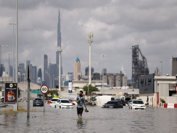 A person walks in flood water caused by heavy rains, with the Burj Khalifa tower visible in the background, in Dubai, UAE (Photo/Reuters)