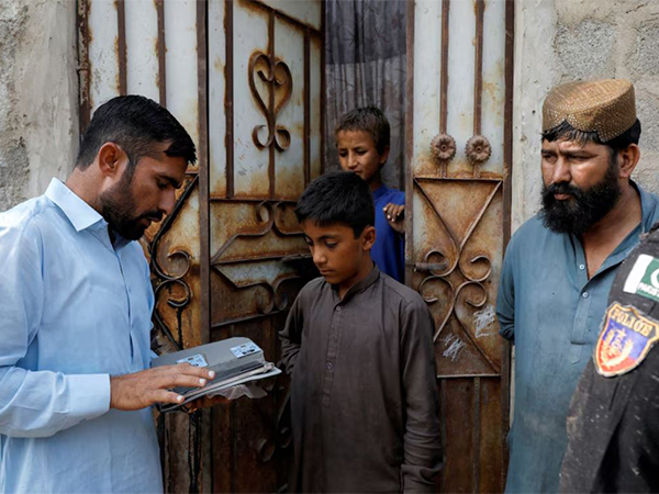 A worker from the National Database and Registration Authority (NADRA), speaks to Afghan citizens while verifying their identity cards on an online tab, during a door-to-door search and verification drive for undocumented Afghan nationals, in an Afghan Camp on the outskirts of Karachi (File Image/Reuters)
