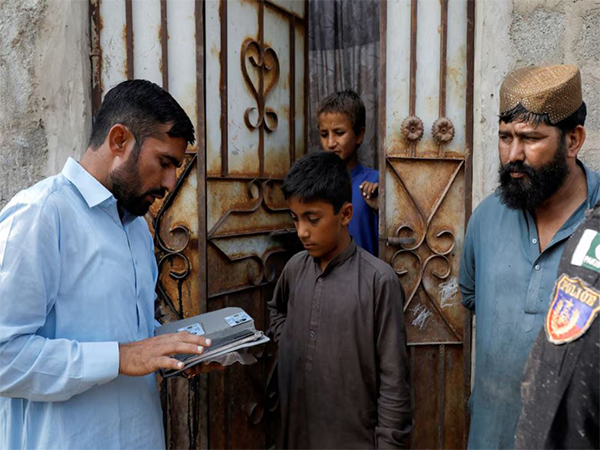 A worker from the National Database and Registration Authority (NADRA), speaks to Afghan citizens while verifying their identity cards on an online tab, during a door-to-door search and verification drive for undocumented Afghan nationals, in an Afghan Camp on the outskirts of Karachi (Image/Reuters)