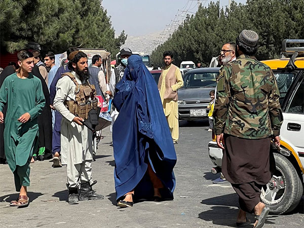 Taliban forces block roads near the airport as a woman in a burqa walks by in Kabul, Afghanistan (File Photo/Reuters)