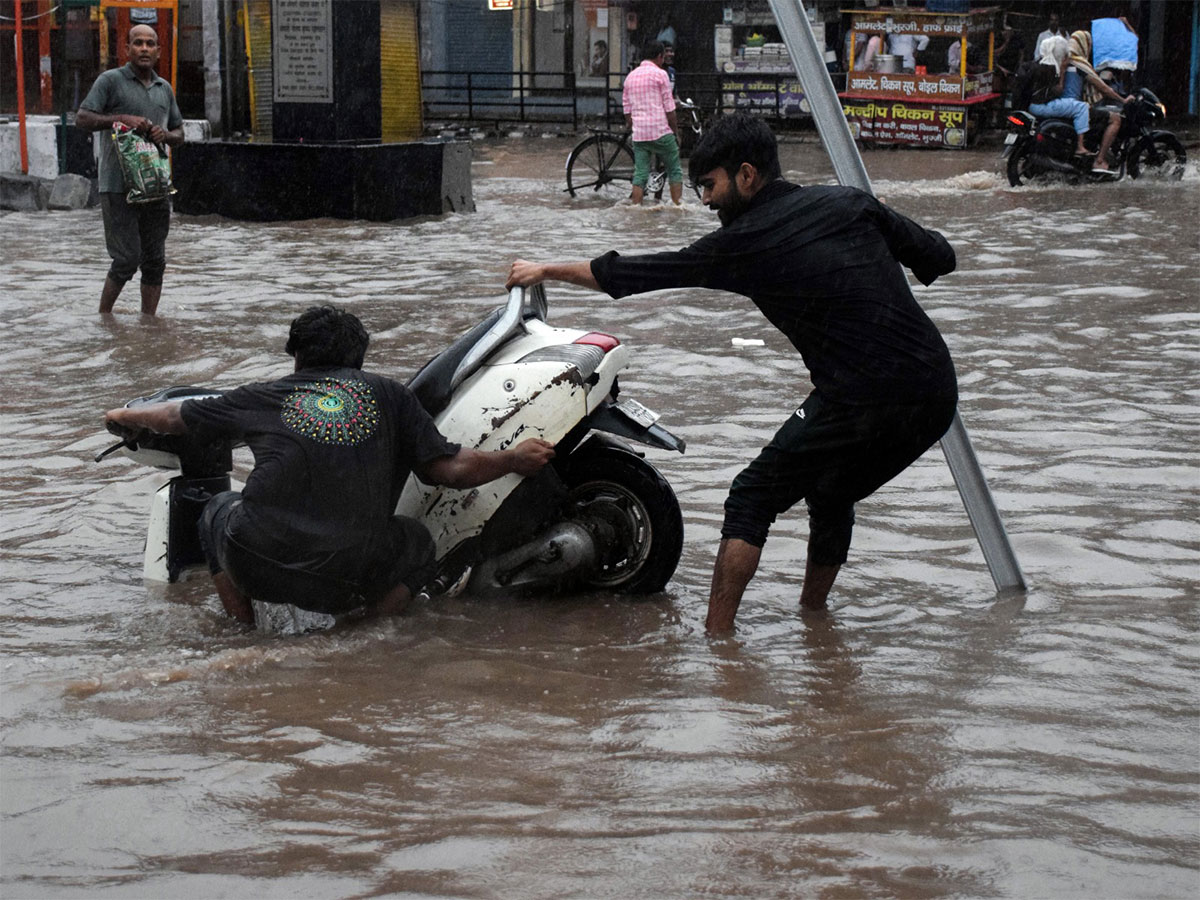 Two men try to pull out the scooter after it gets stuck on a waterlogged road amid rain, in Delhi on Monday (Photo/ANI)