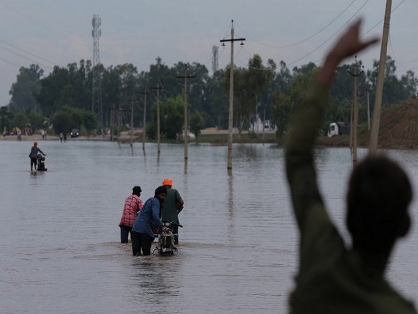 Commuters wade their way through waterlogged roads in the flood-affected area (Photo/ANI)