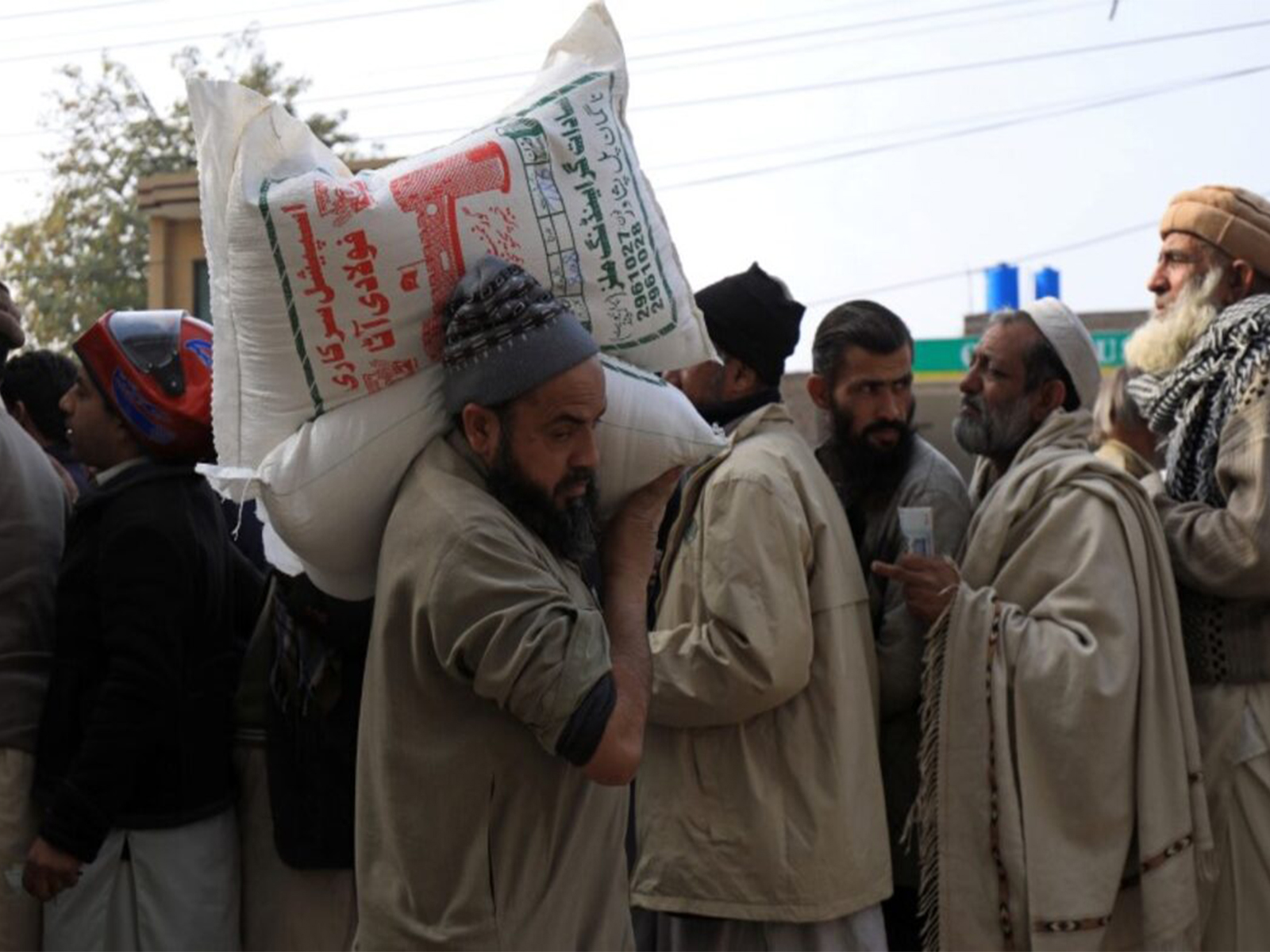 A man carries sacks of flour on his shoulder, while others stand in queue to purchase from a truck ( File Photo/ Reuters)