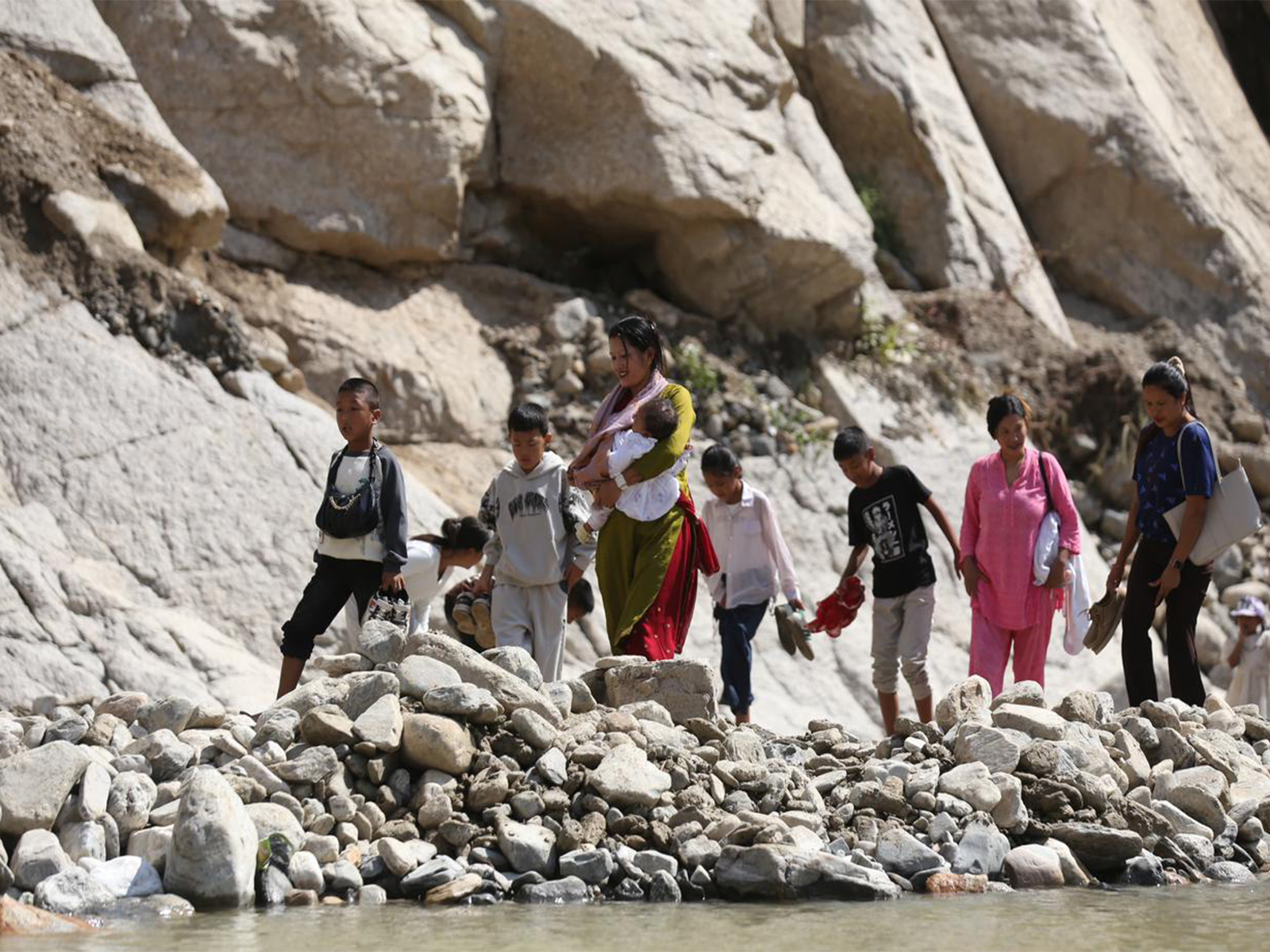 People, including women and children, cross a damaged section of the BP Highway in Nepal by wading through the Roshi River after heavy rains washed away road diversions, disrupting travel across the region. (Photo/ANI)
