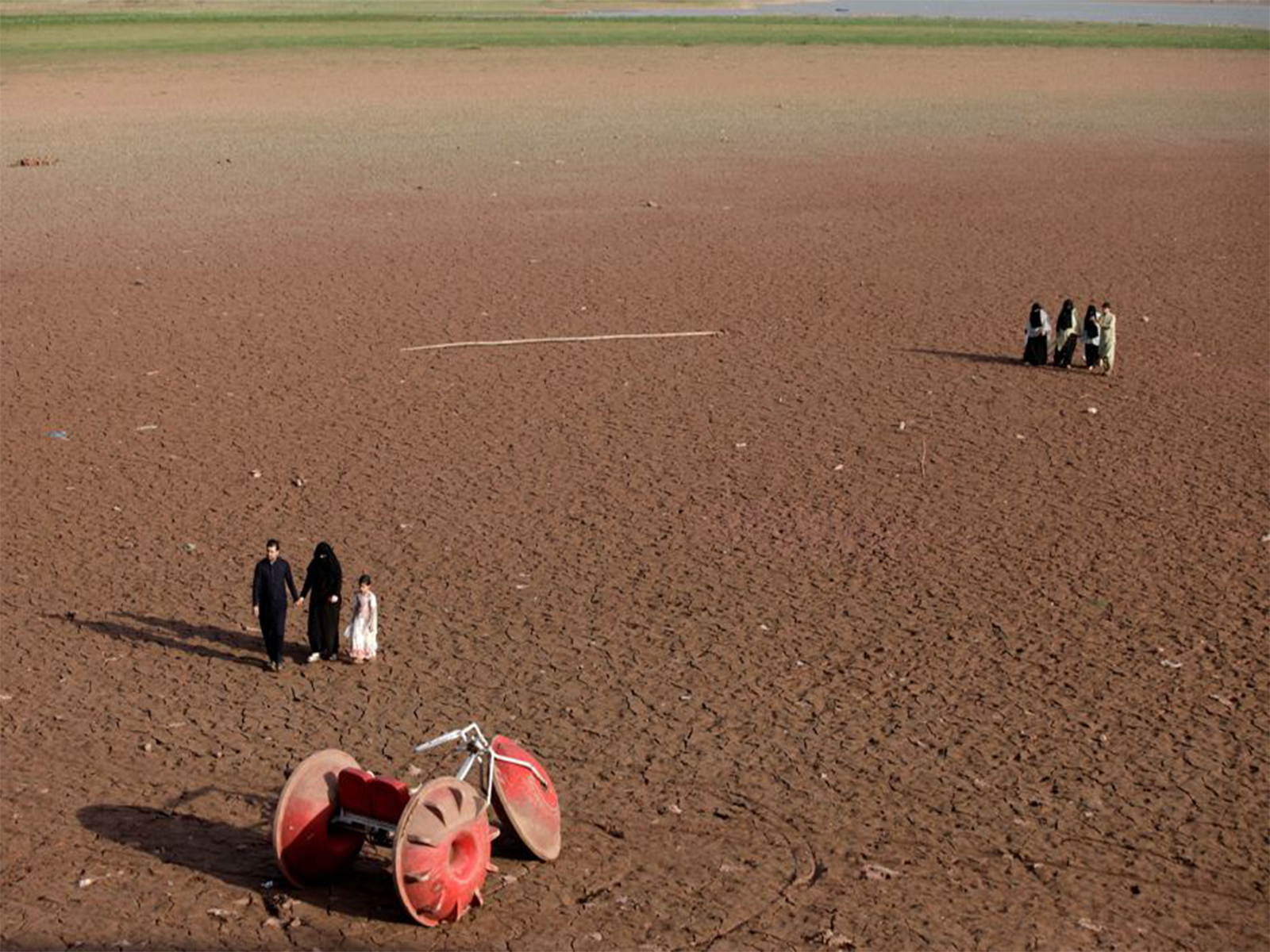   People walk near a three-wheeler parked at a dry portion of land that used to have water in Pakistan (File Photo/ Reuters)