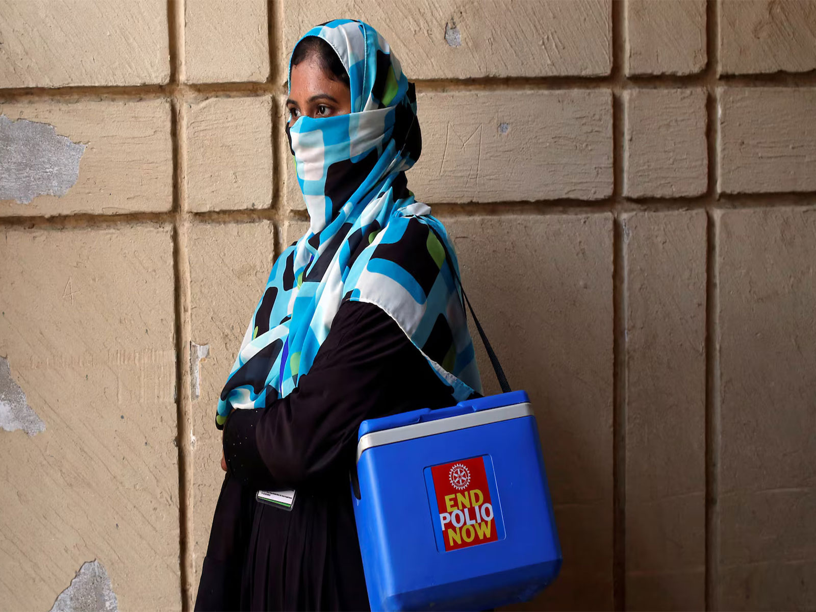 A polio vaccinator carrying a kit box waits for fellow workers during an immunisation drive in a low-income area of Karachi. (Photo/Reuters)