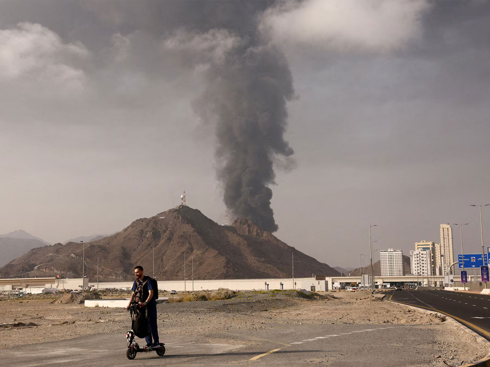A person rides a scooter as smoke billows from the Fujairah Oil Industry Zone after debris from a drone intercepted by air defences triggered a fire, in Fujairah, United Arab Emirates (Photo/Reuters)