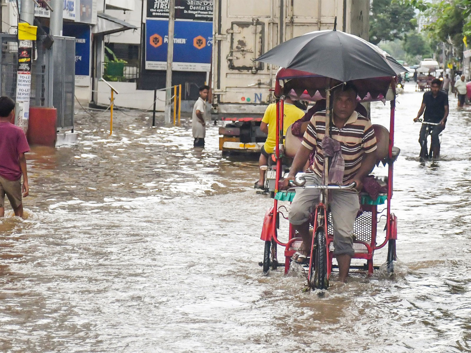 A rickshaw puller and other commuters wade through knee deep water in Guwahati (Photo/ANI)