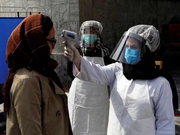 Afghan health worker in protective gear checks the temperature of a woman in Kabul