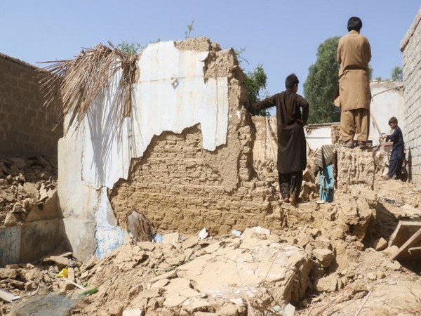 Residents stand amid the rubble of a damaged house following an earthquake in Harnai, Balochistan