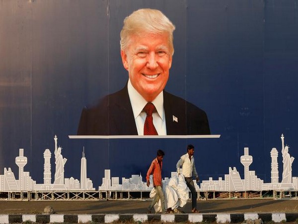 Workers walk past a hoarding of U.S. President Donald Trump in Ahmedabad