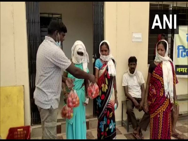 A village official hands out tomatoes to people lining up to get vaccinated. (Photo/ANI) 