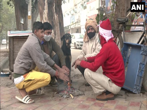 People sit near the fire to comfort themselves as temperatures drop in Delhi on Saturday. [Photo/ANI]