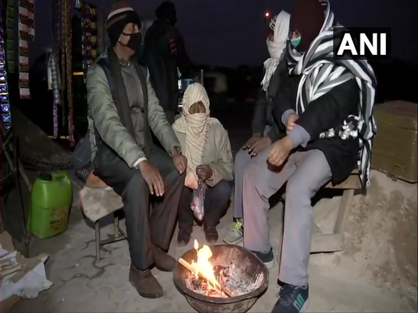 People were seen sitting near the fire on Sunday in Delhi's Anand Vihar area. (Photo/ANI)