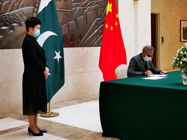 Pakistan President Arif Alvi writing remarks in Chinese embassy's visitor's book in presence of Charge d' Affaires Pang Chunxue