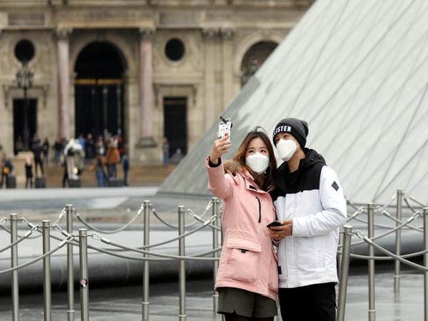 A couple wearing masks poses for a selfie near the Louvre Pyramid in Paris, France