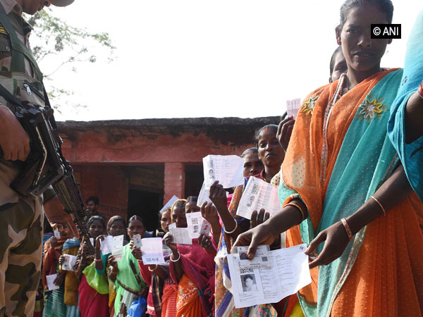 Women voters line up at a polling station as security person stands guard in Jharkhand. 