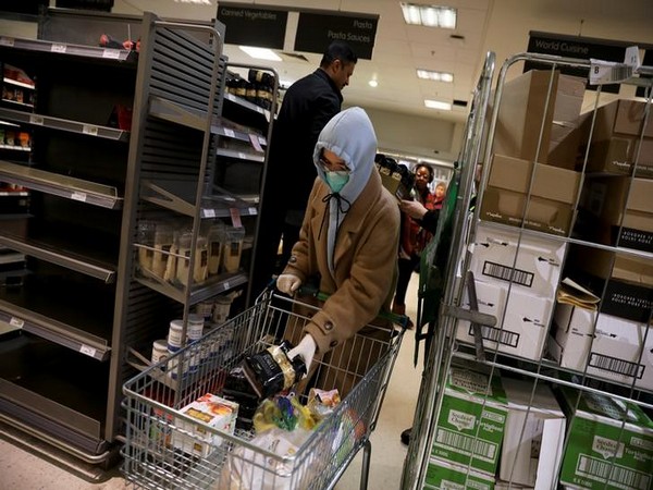 A woman wearing a protective mask puts a bag of pasta in her shopping cart at supermarket Waitrose in London