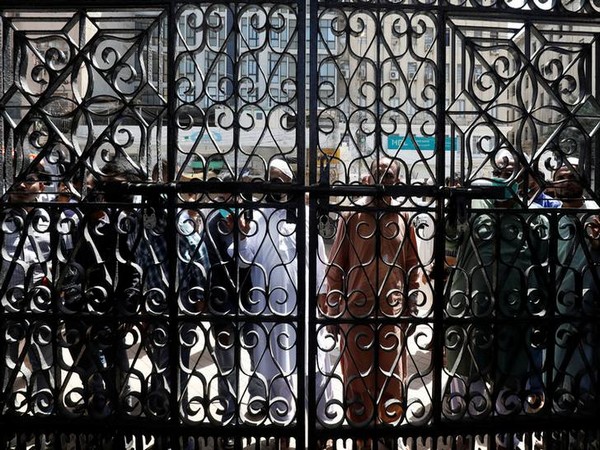 People stand outside the locked entrance gate of a mosque as they arrive to attend Friday prayer despite a lockdown