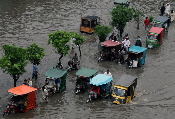 Commuters on rickshaws and motor vehicles pass through floodwaters after rains lash Karachi  