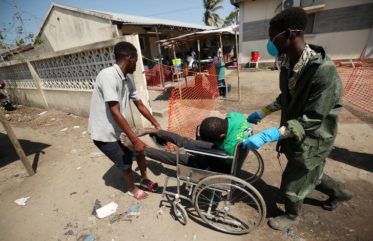 A medical staff member wears a protective mask as he assists a man arriving at a cholera treatment centre set up in the aftermath of Cyclone Idai in Beira, Mozambique