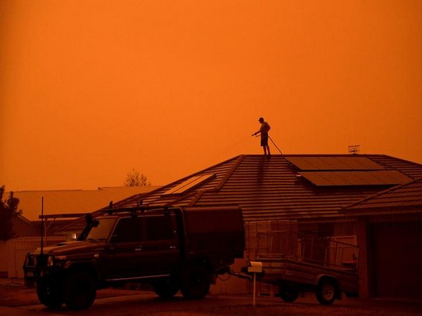A resident uses a garden hose to wet down the house as high winds push smoke and ash from the Currowan Fire towards Nowra, New South Wales.