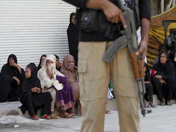 A policeman stands guard as Shi'ite Muslim women watch a Muharram procession ahead of Ashura in Peshawar, Pakistan