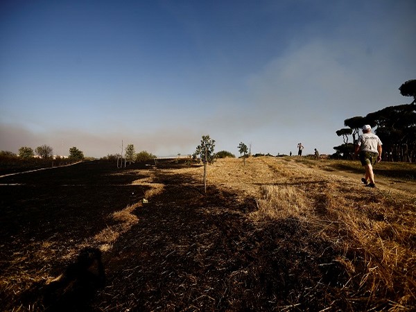 People walk in a burned park, as smoke rises from a forest fire, in north Rome, Italy, July 4, 2022. (Photo Credit: REUTERS)