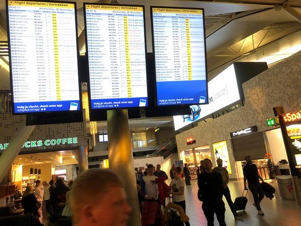 People look on and walk next to a flights information board inside the terminal of Amsterdam's Schiphol airport