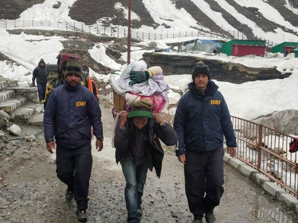 SDRF personnel helping the devotees cross snow-laden paths in Kedarnath. Photo: ANI.