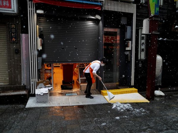 A shop employee wearing a protective face mask following an outbreak of COVID-19 tries to remove snow in Tokyo, Japan March 29, 2020. 