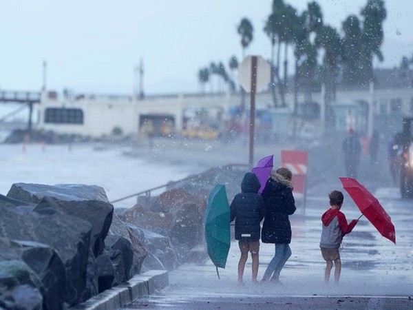 Kids use umbrellas for protection from the crashing waves of a high tide as a winter storm arrives in Oceanside, California