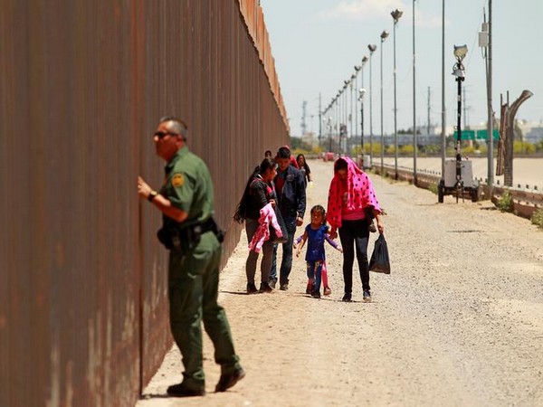 A group of Central American migrants walk next to the US-Mexico border fence after they crossed the borderline while a Border Patrol agent looks through the fence in El Paso, Texas.