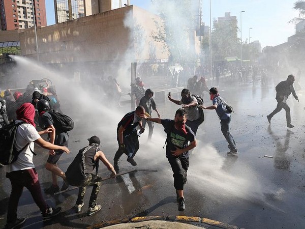 Demonstrators run as a riot police water cannon sprays water during a protest against Chile's state economic model in Santiago