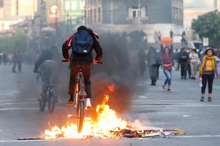 A demonstrator cycles over burning objects on a road during a protest against the government in Valparaiso