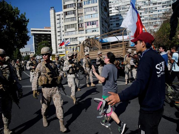 A demonstrator gestures as Chilean soldiers advance carrying their weapons, during a protest against Chile's state economic model in Santiago
