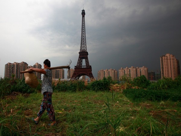 A Chinese farmer carrying a rake walks down a dirt road past a replica of the Eiffel Tower at the Tianducheng development in Hangzhou, Zhejiang Province, China. (Image credit: Reuters)