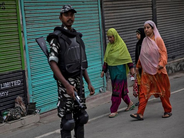 Kashmiri women walk past an Indian security personnel during restrictions in the region