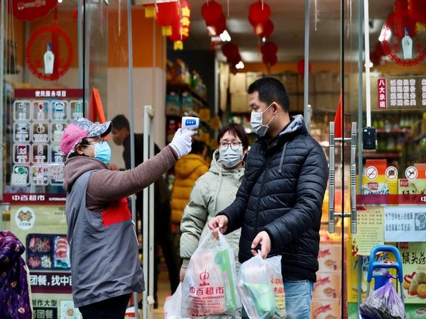 A worker measures temperature of people leaving a supermarket in Qingshan district following the coronavirus outbreak in Wuhan