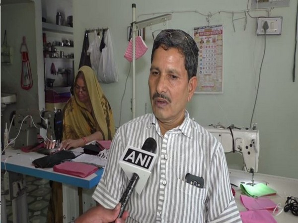 Hanuman Prajapat talking to ANI, with wife Ratna ben stiching masks in background (Photo/ANI)