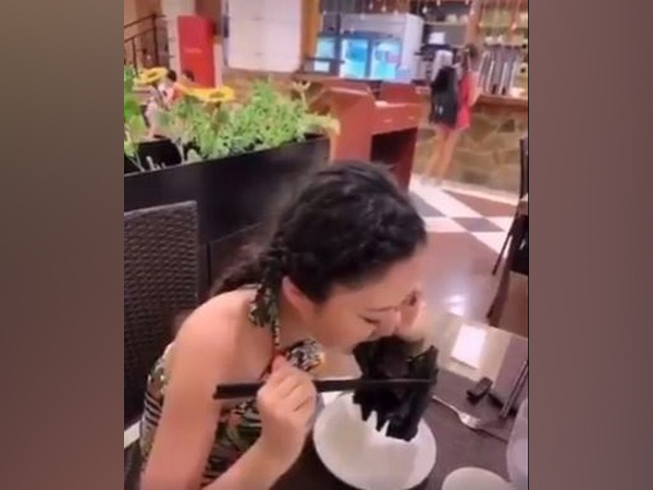 The woman can be seen biting through what appears to be a fruit bat which is held to her mouth with a pair of chopsticks (Picture Courtesy: Twitter)