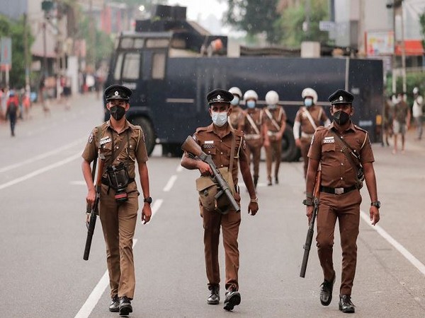 Sri Lankan police officers with tear gas guns walk along a road as people protest (Photo Credit: Reuters)