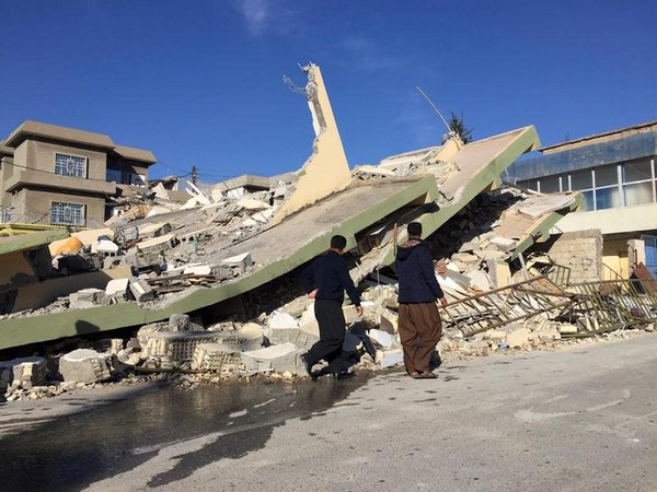 People walk past a damaged building following an earthquake in Iraq in 2017